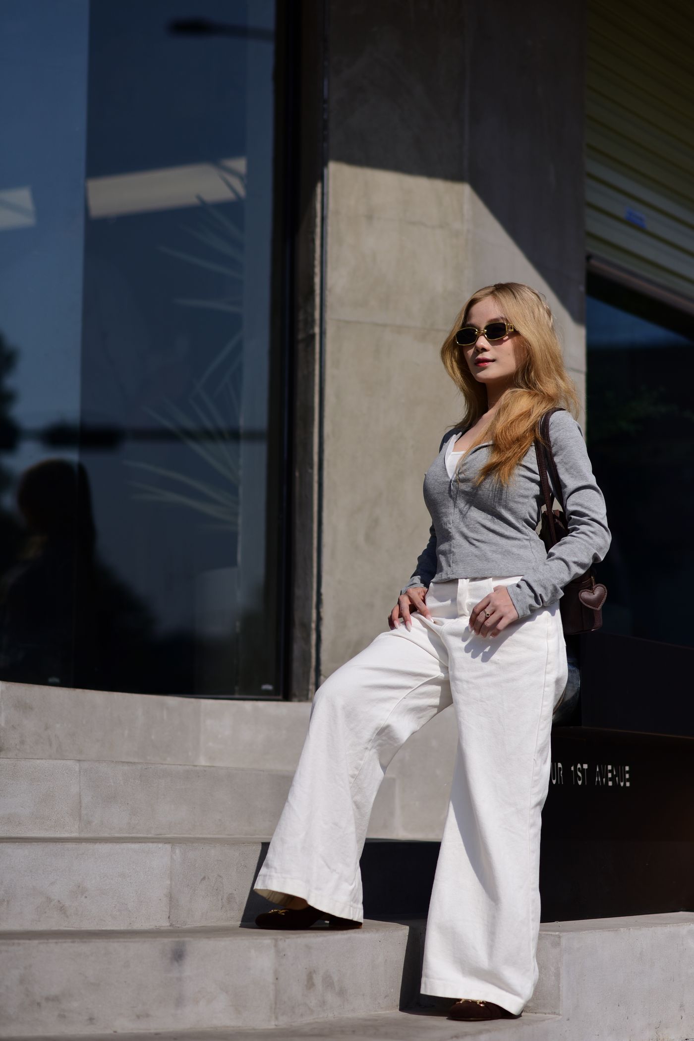 Woman in a fitted grey top and white wide-leg trousers on stone steps.