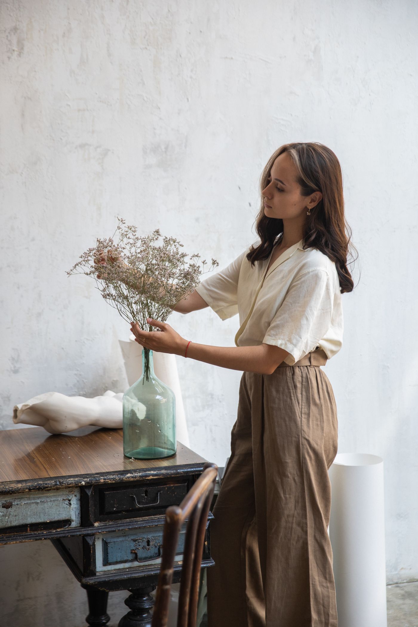 Woman wearing a loose linen shirt and trousers while arranging flowers.