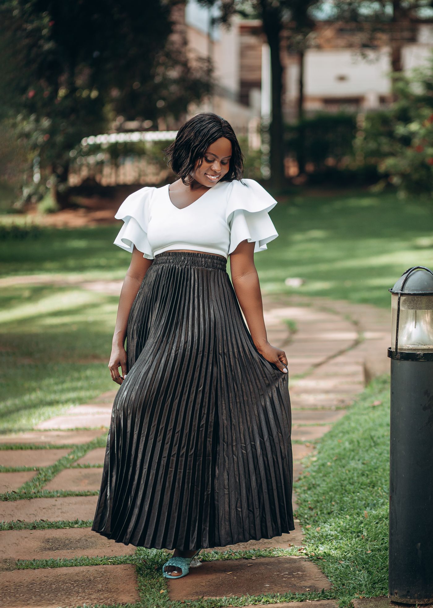 Woman wearing a white flutter-sleeve top, long pleated skirt and flat shoes.