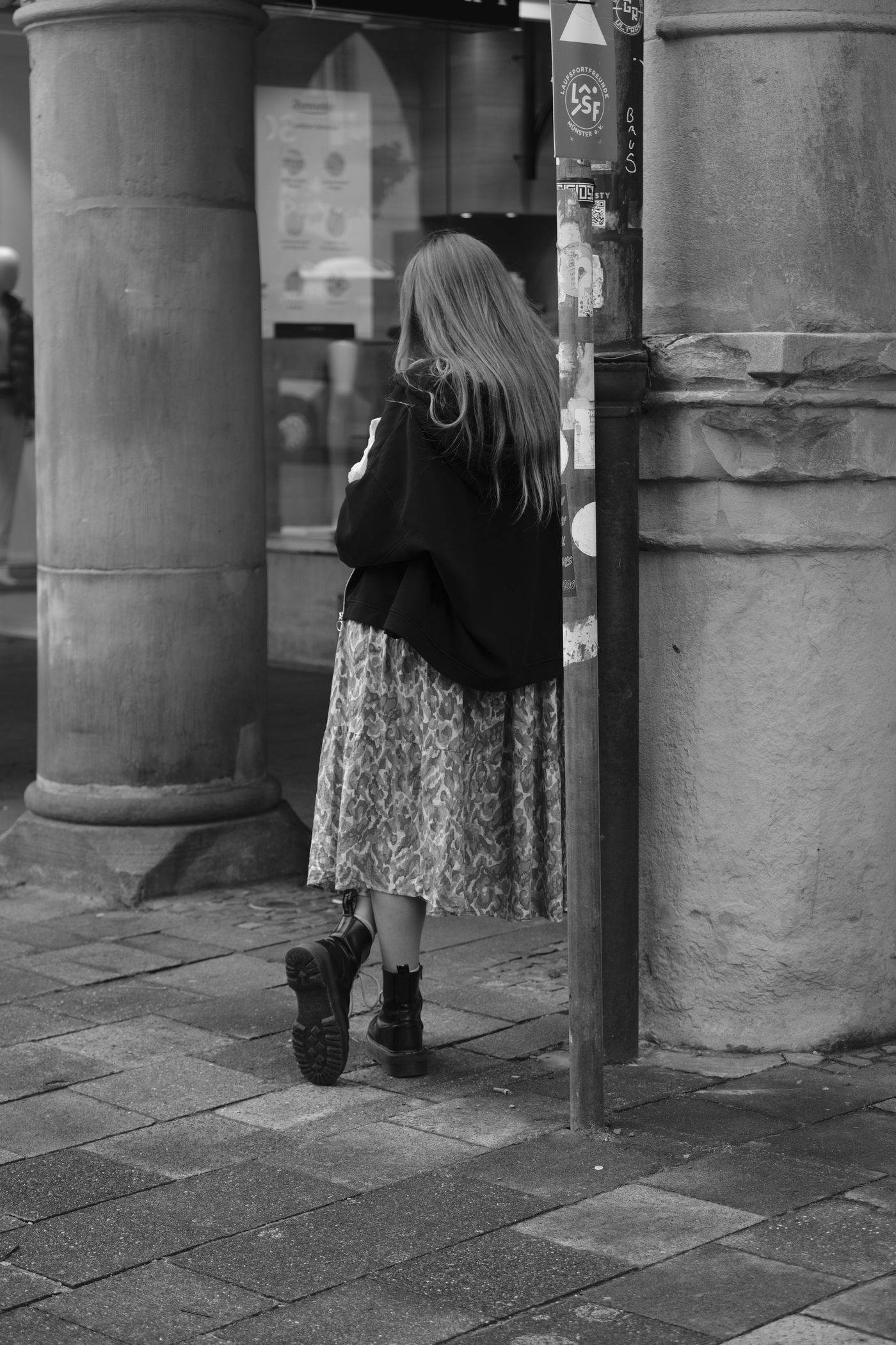 Woman in a dark cardigan and patterned midi skirt on a pavement.
