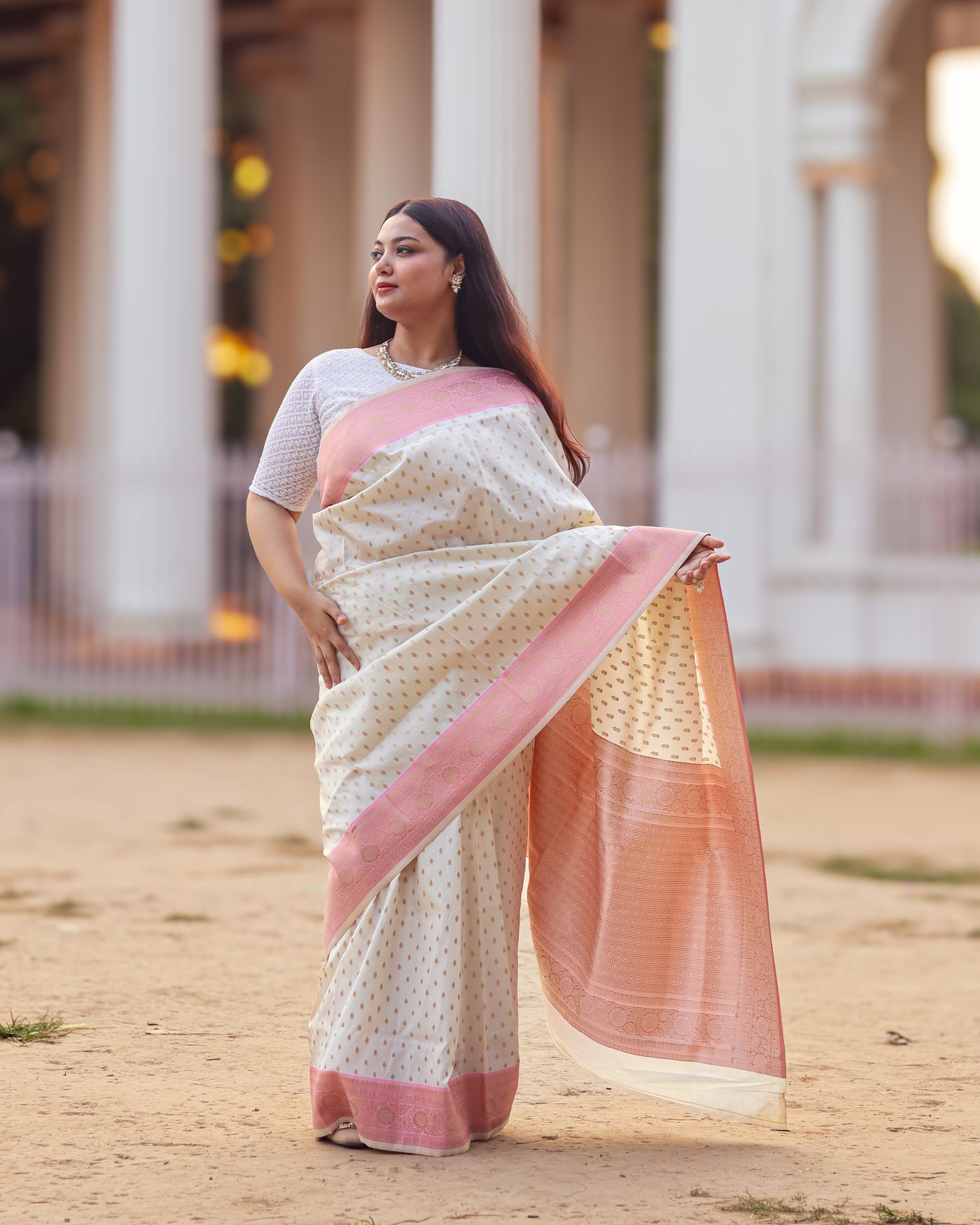 Woman wearing a cream and pink saree with a loose pallu outdoors.