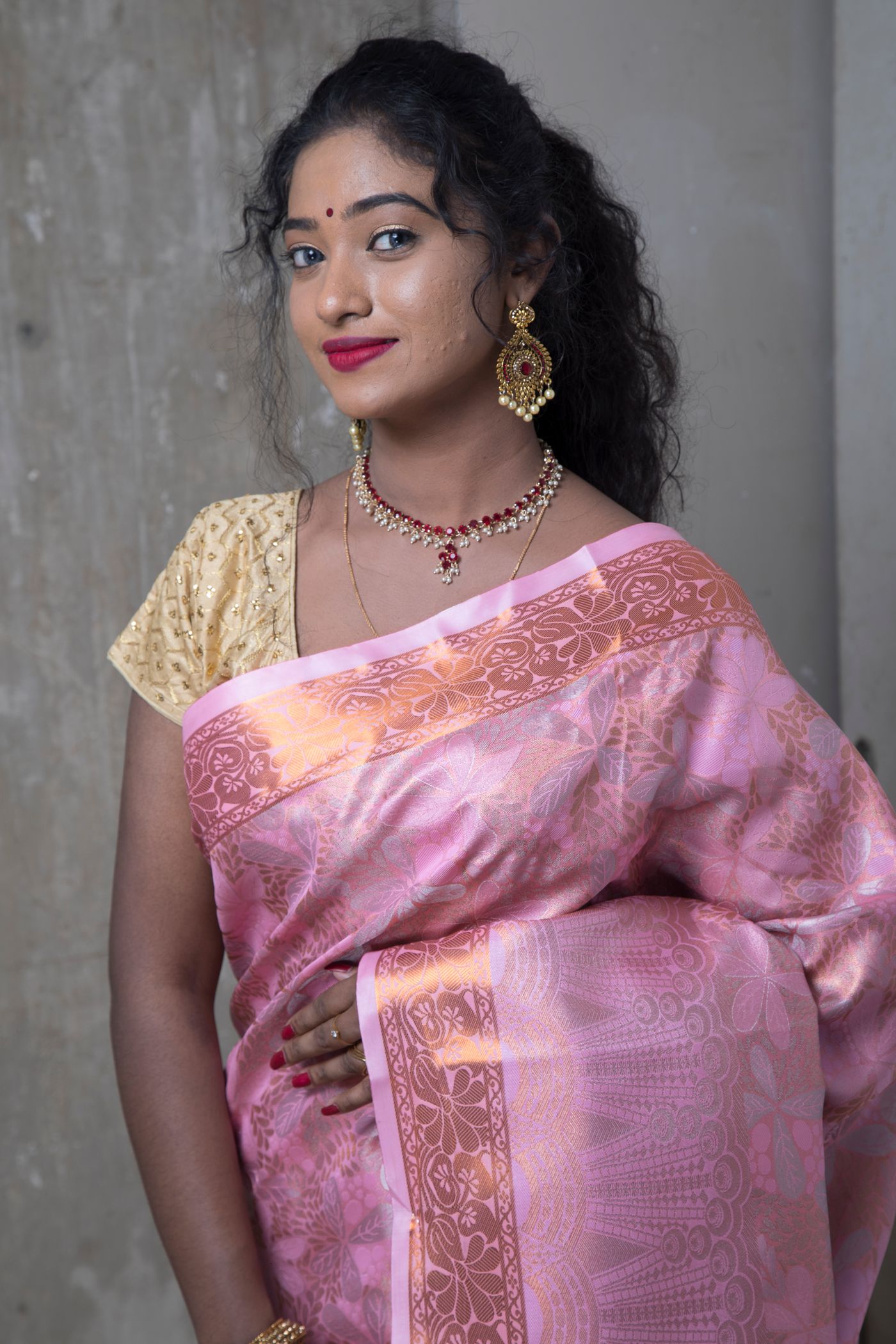 Woman wearing a pink floral saree with a gold blouse and drop earrings.