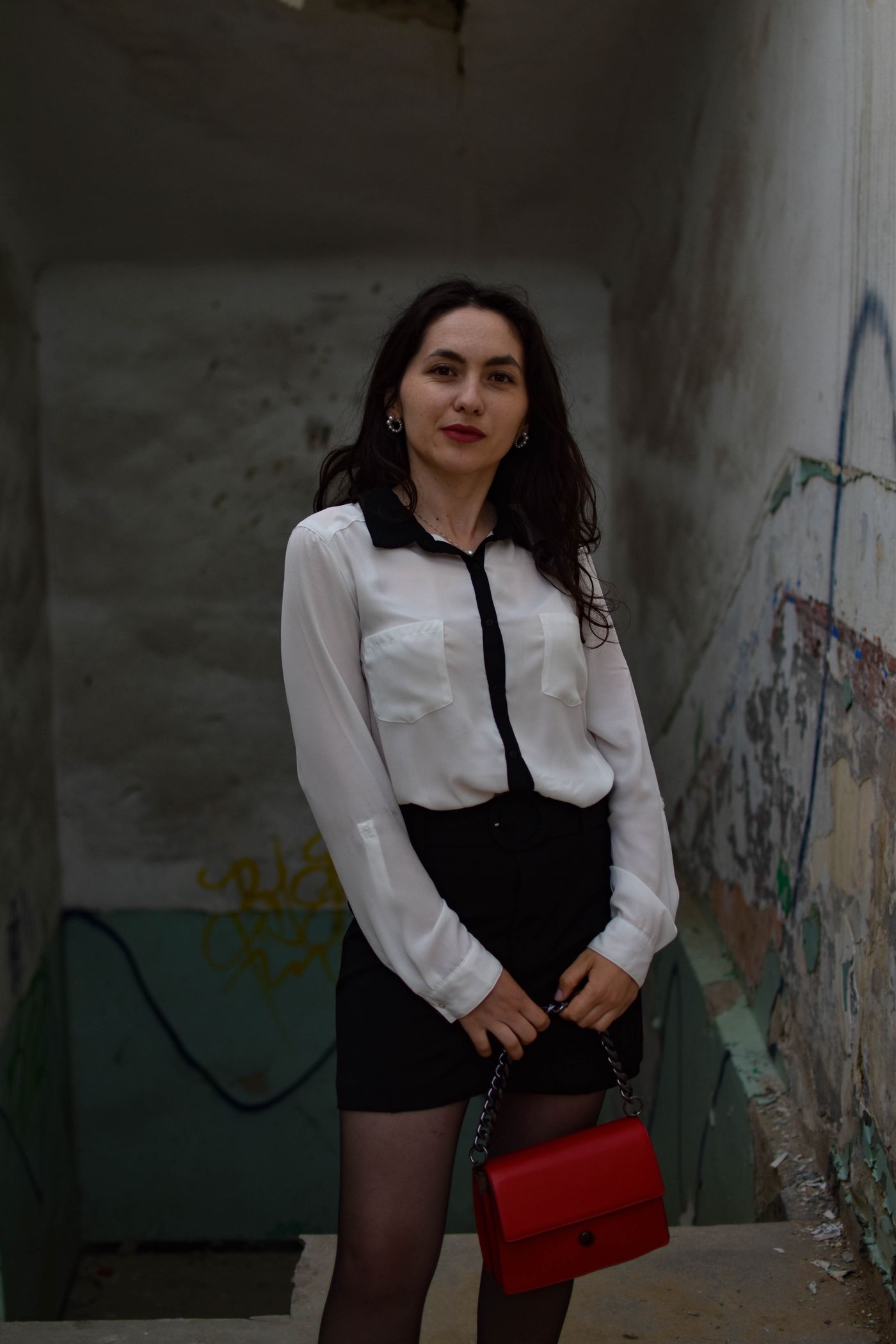 Woman carrying a red handbag with a white shirt and black skirt.