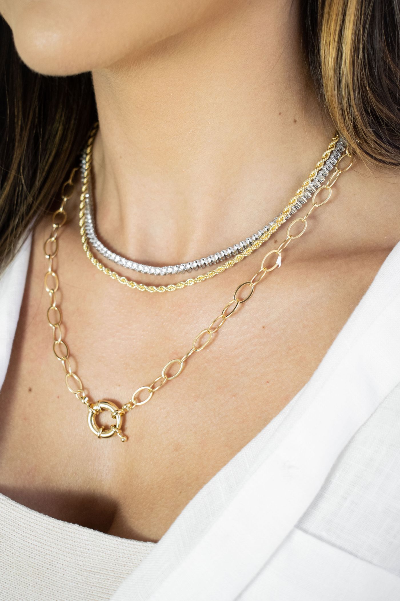Layered gold-tone and silver-tone chains worn above a white neckline.