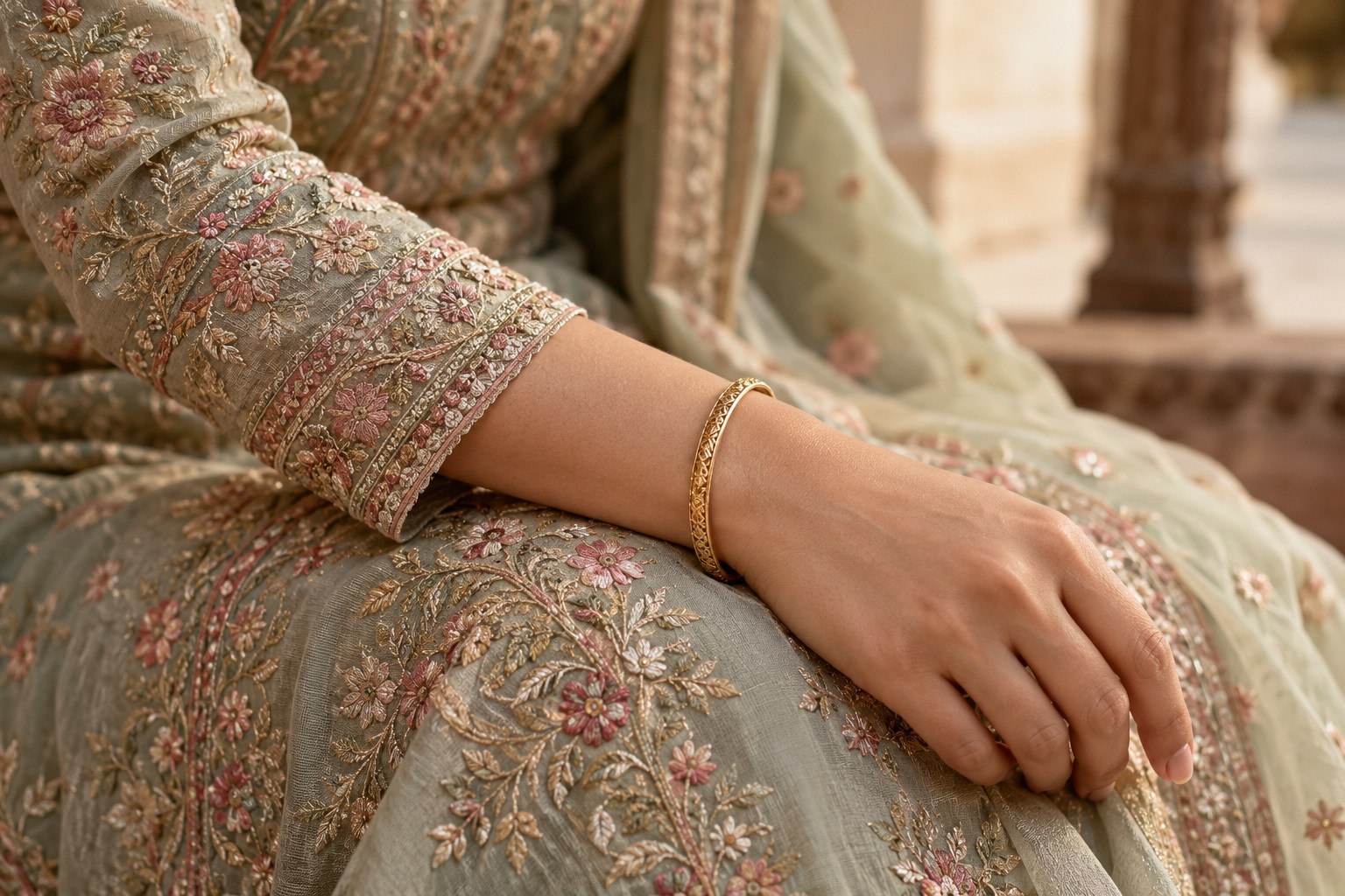 Close-up of an adult woman's embroidered long sleeve ending above one slim bangle, restrained jewellery.