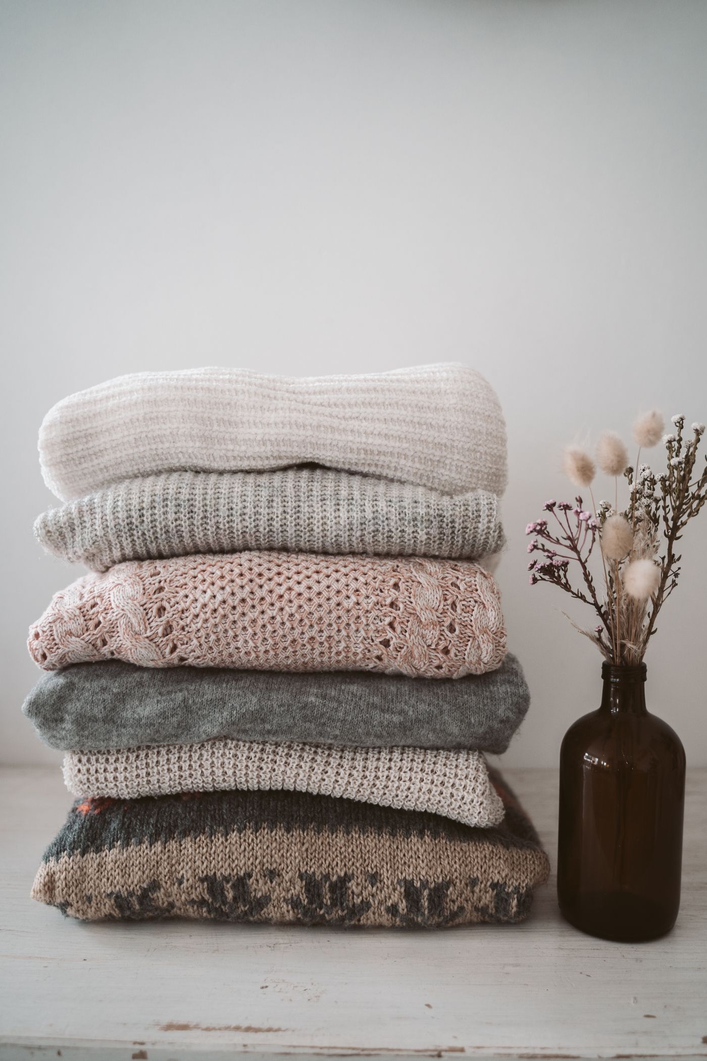 Stack of folded knitted sweaters in muted colours.