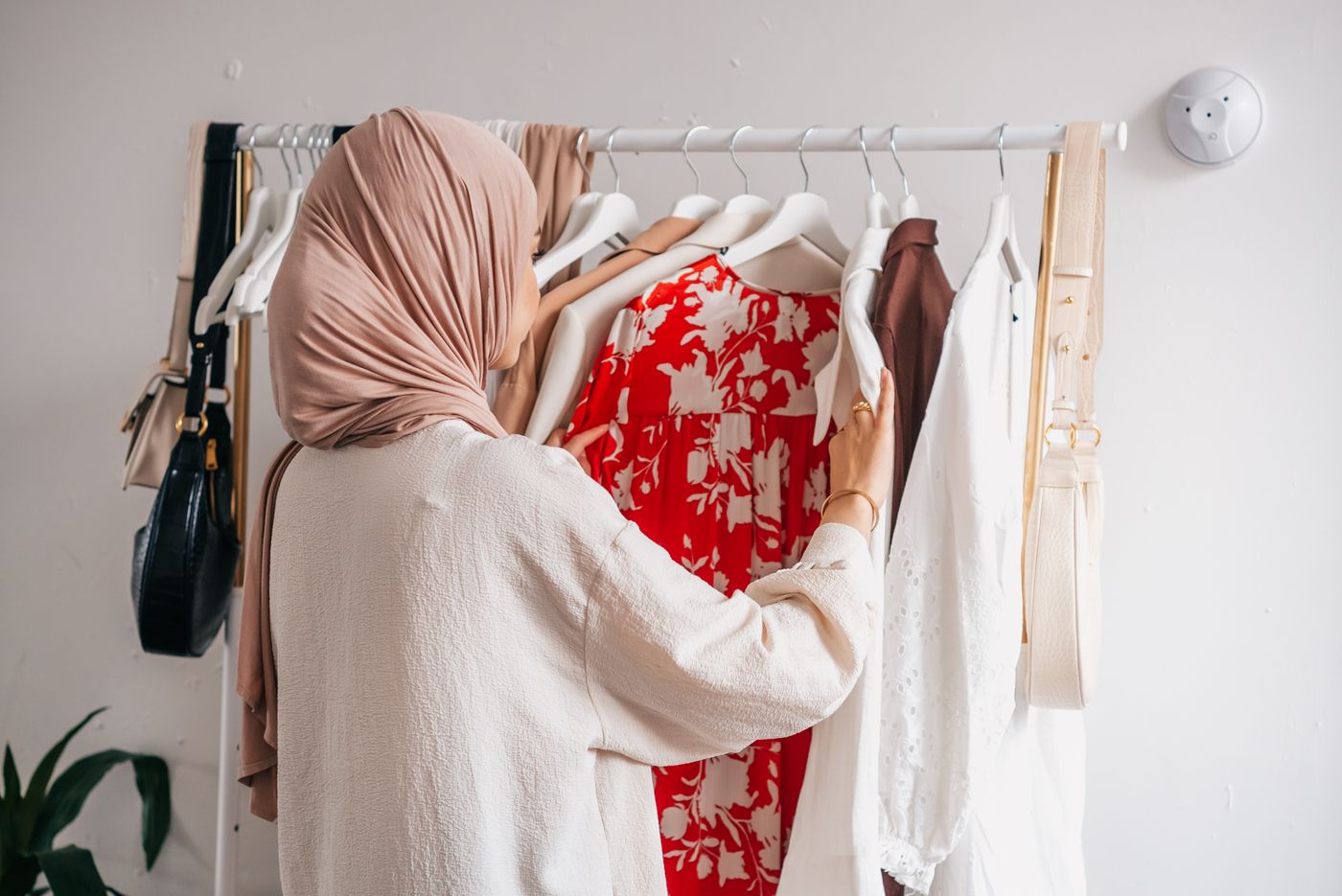 Woman examining a floral garment beside a rail of clothes.